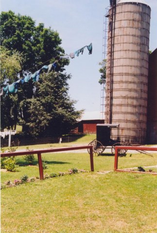 Clothes hanging to dry on a line connected to silo with an Amish buggy